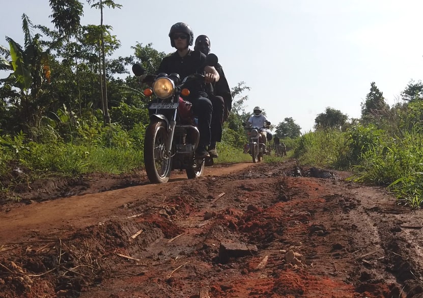 Das Projektteam auf Motorrädern auf einer ausgefahrenen Lehmpiste unterwegs zu den Dörfern
