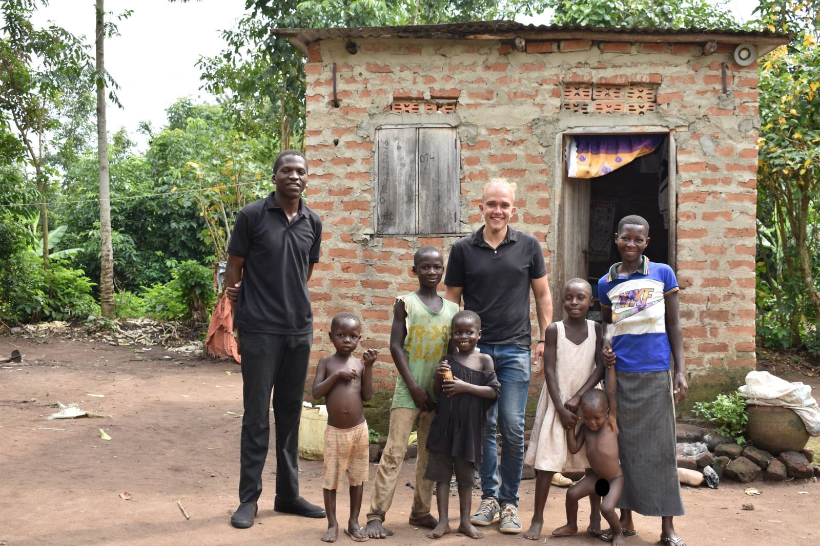 Direct Transfers Team mit einer Familie vor ihrem Haus in Uganda